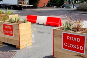 Photo showing two large wooden planters with "road closed" signs on.