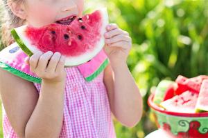 photo of a young girl eating a slice of watermelon outside