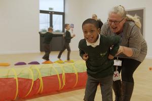 photo of a young schoolboy being helped by a member of school staff during a fun activity