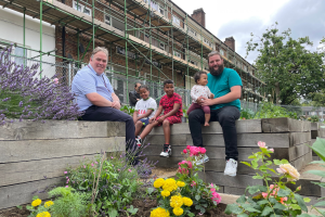 Mayor Perry with a family sitting on raised planters outside a housing block