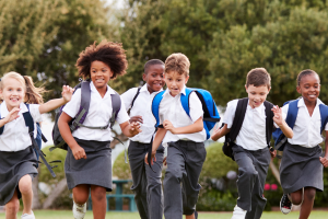 A group of schoolchildren in uniform, running with backpacks