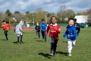 A group of young children running happily across a sports field