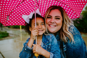 A woman and child beneath a red and white polka dot umbrella outside