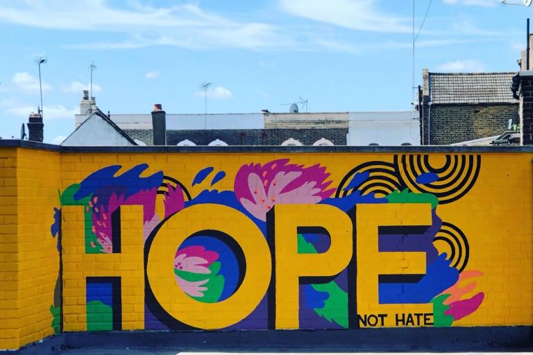 A mural painted on a wall saying 'Hope' in yellow letters with a yellow, blue, pink and green background