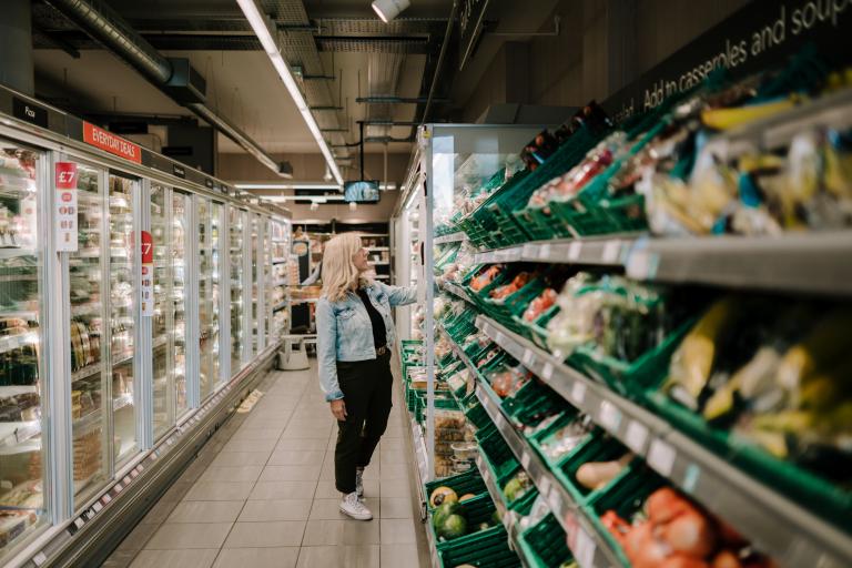 A woman standing in a supermarket aisle looking at produce.