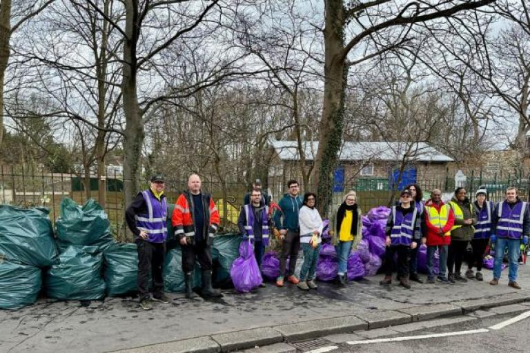 A group of people holding rubbish sacks standing next to a large pile of filled rubbish sacks
