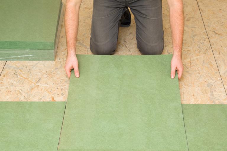 A person laying green natural wood fiber insulation board on a floor..