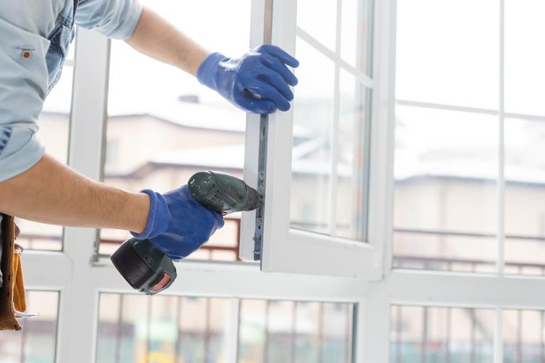 A person in protective clothing installing white UPVC plastic window indoors.