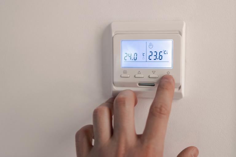 A person adjusting the controls on a wall mounted heating thermostat.