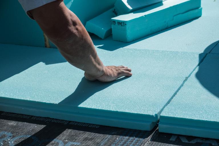 A roofer placing energy saving XPS polystyrene insulation boards on a flat roof.