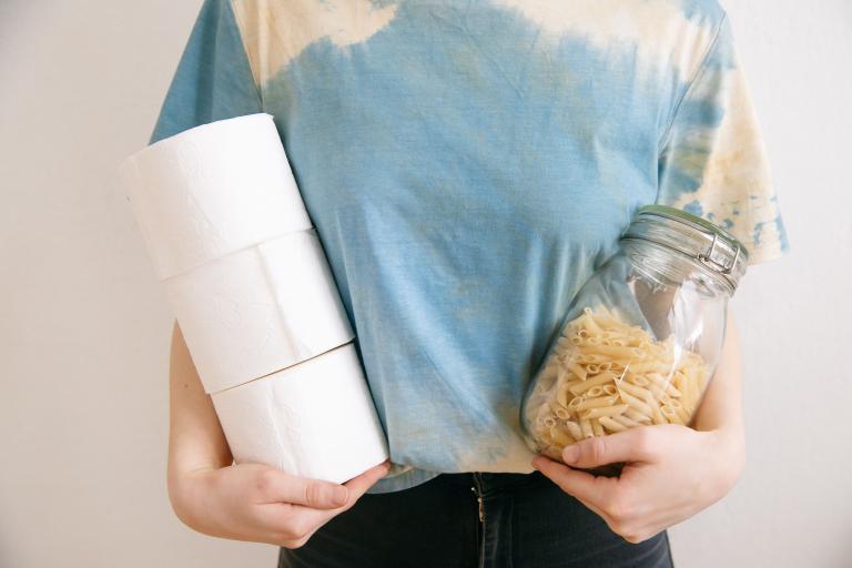 A person holding a jar or pasta and toilet roll
