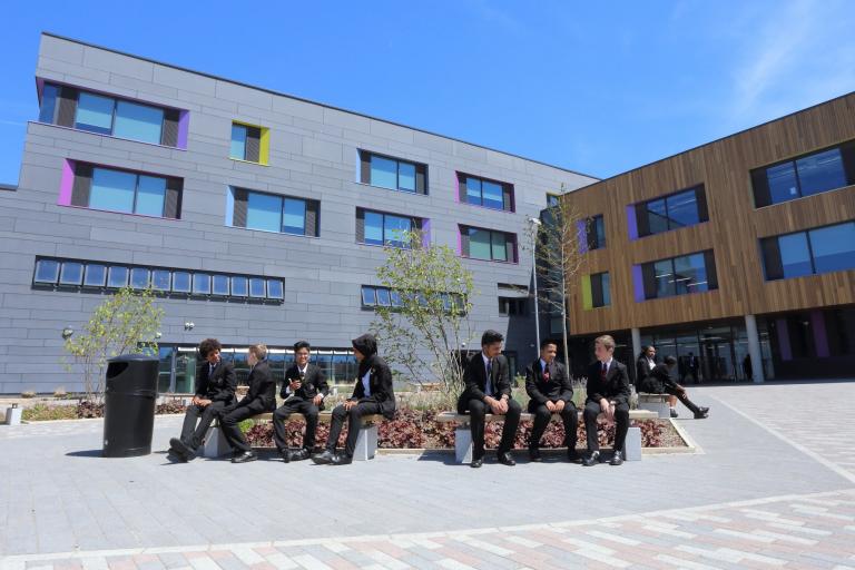 school building with pupils seated outside